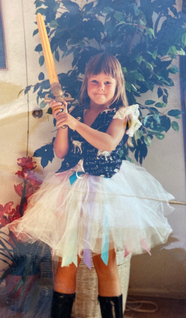 Blond little girl wearing a tutu, boots, and vest while holding a toy sword.